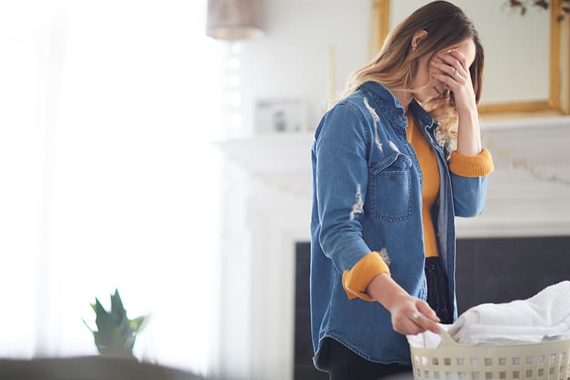 A Christian woman with her laundry basked and her head in her hands because she needs to replace grumbling with gratitude
