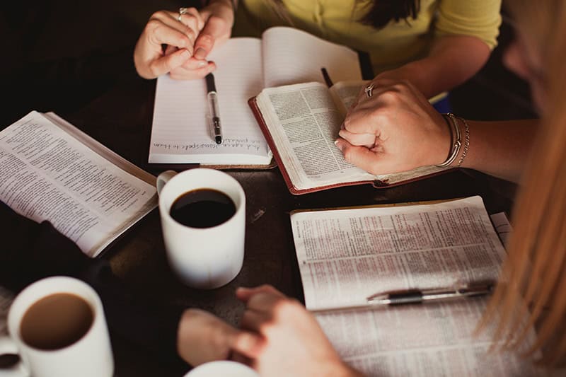 A group of Christian women holding hands around the table in connection over Bible study and prayer