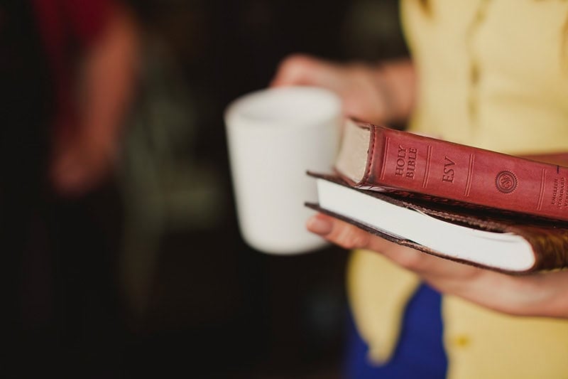 A Christian woman holding a journal, Bible, and a coffee mug