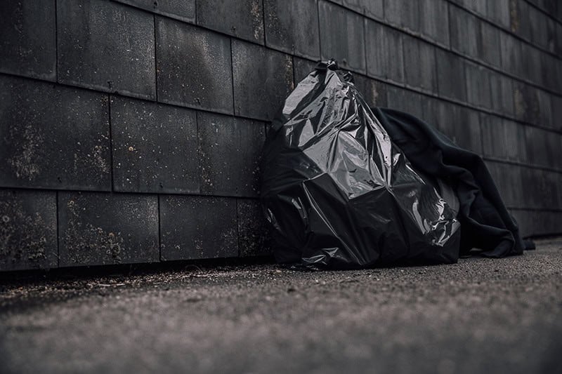 a black garbage bag laying against a brick wall on a sidewalk