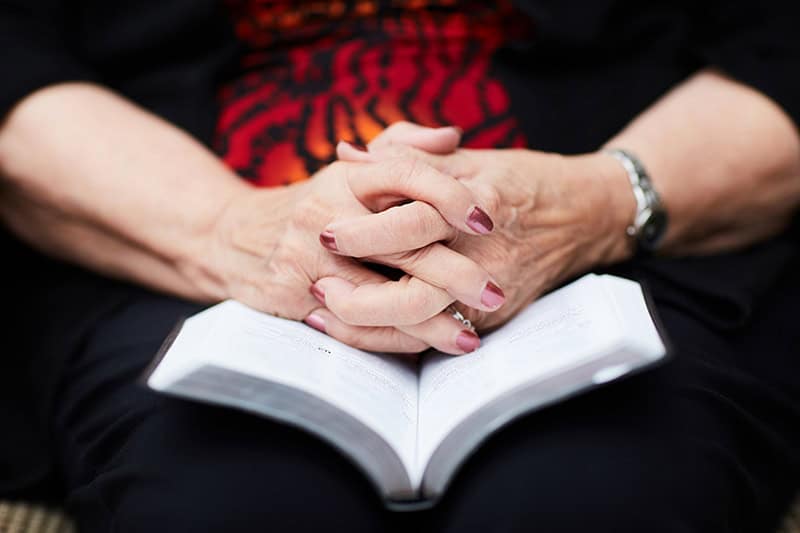 A Christian woman with her hands folded on top of her open Bible as she prays to be a vessel to convey the power of love