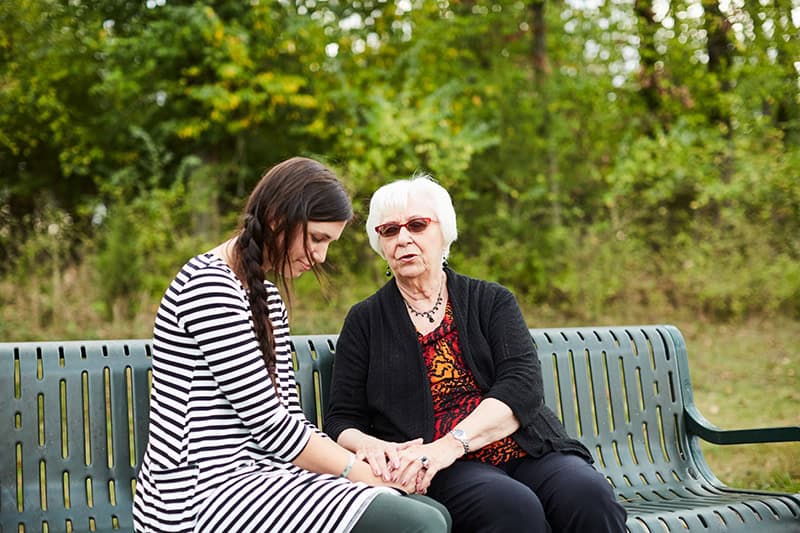 Two Christian women sitting on a park bench, holding hands, and enjoying the power of love
