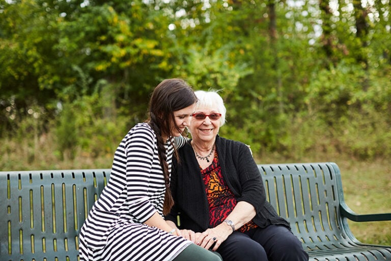 Two smiling Christian women sitting on a park bench enjoying the power of love