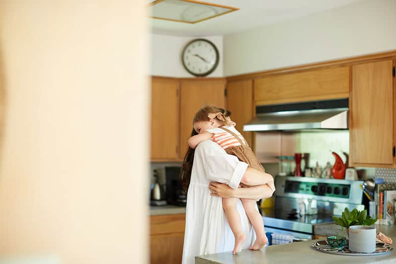 A Christian mom holding and hugging her toddler daughter in her kitchen