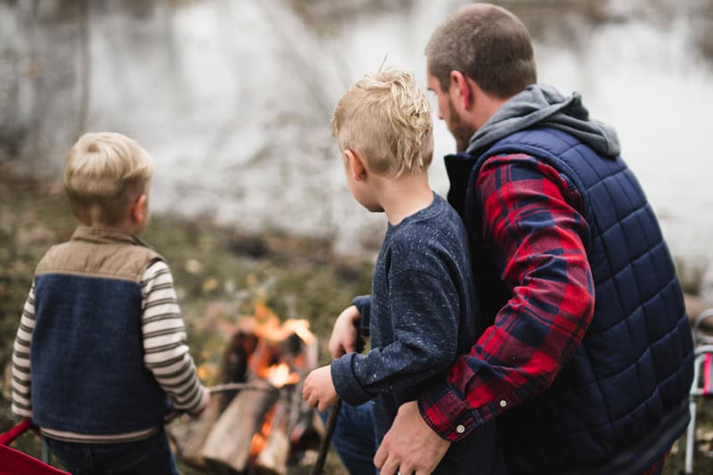 A Christian dad with his two young sons at a campfire as he aims to pass down your faith to the next generation