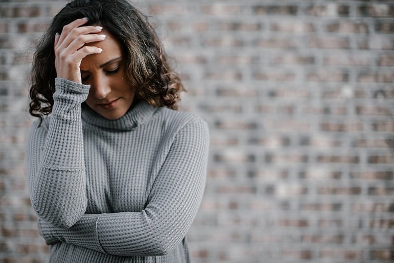 A Christian woman with her head in her hand, wondering how to trust God in difficult seasons