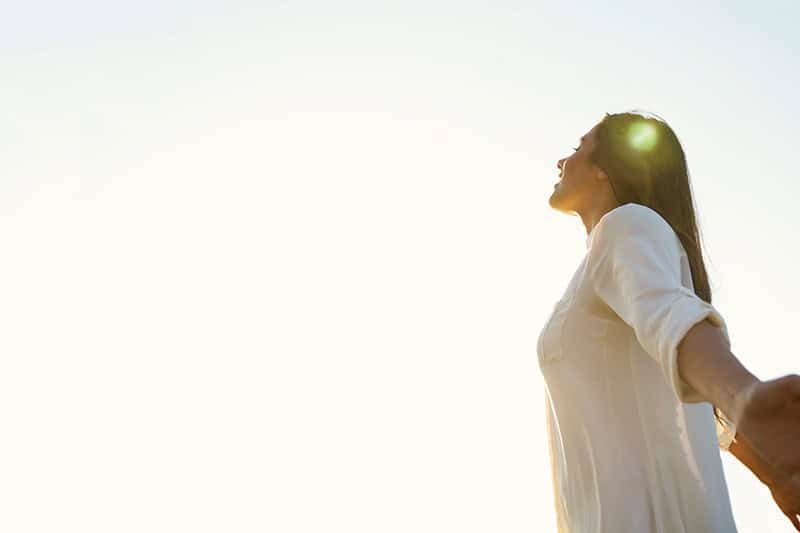 A Christian woman with her arms spread wide open and her head turned toward the sky in gratitude for learning to trust God in difficult seasons