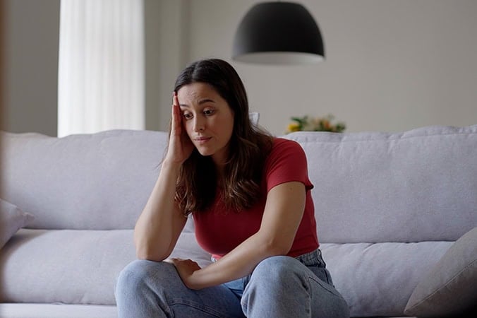 A Christian woman sitting on a couch with her head leaning on her hand, wondering how to transform anxiety into peace