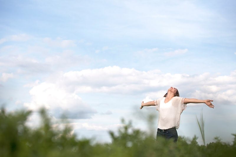A Christian woman outside with her arms opened wide and her head lifted high in biblical thankfulness