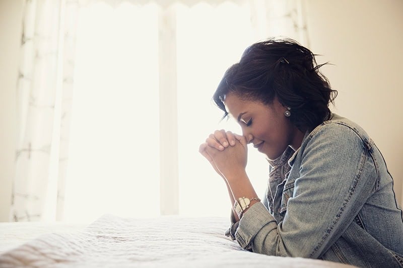 A smiling Christian woman with her head bowed in a prayer of biblical thankfulness