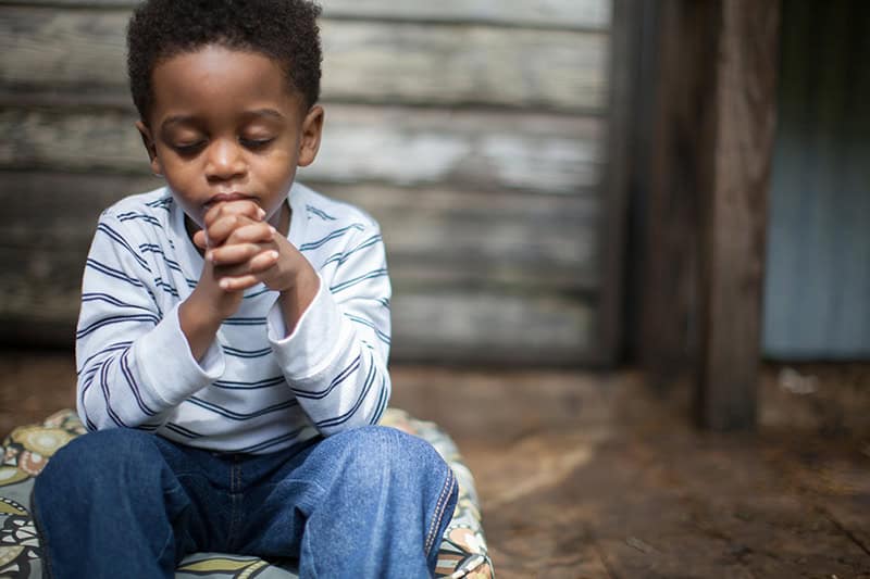 A young boy with hands folded and eyes closed in prayer