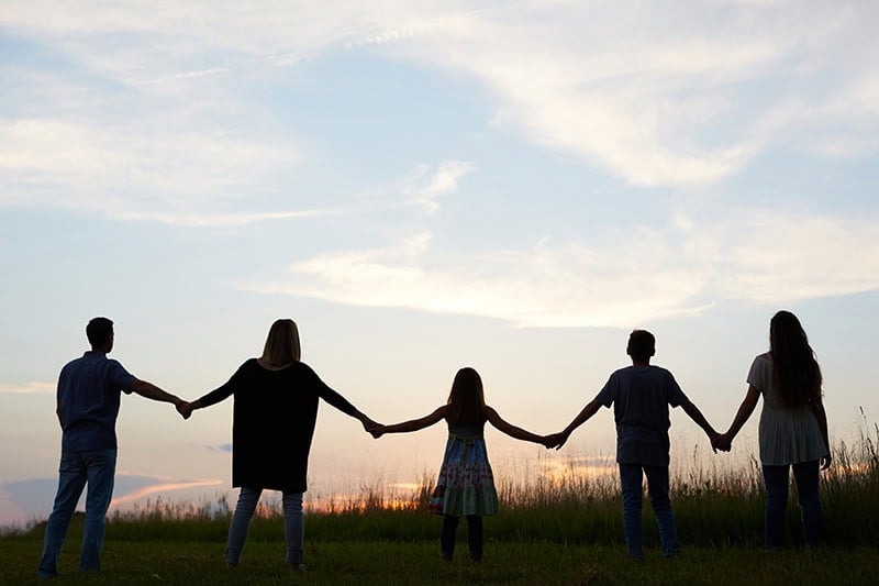 A family with a Christian mom, Christian dad, and three children, holding hands and facing the sunset