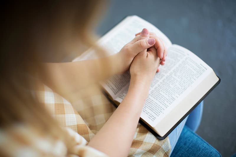 A Christian woman with her hands folded on top of her open Bible as she seeks her identity in Christ as a mom