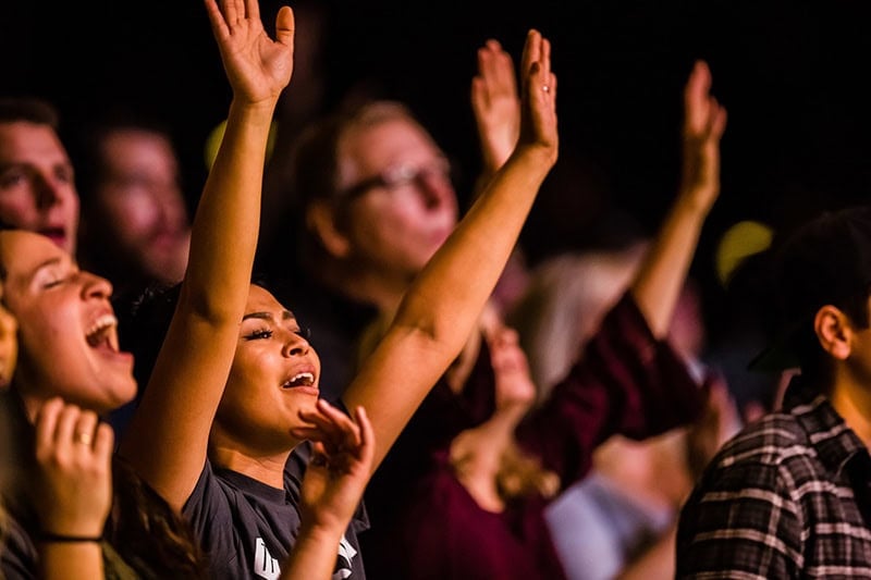 A group of Christians with arms raised as they bless the Lord in worship