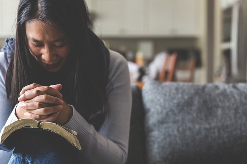 A Christian woman with her hands folded and her head bowed in a prayer for difficult times