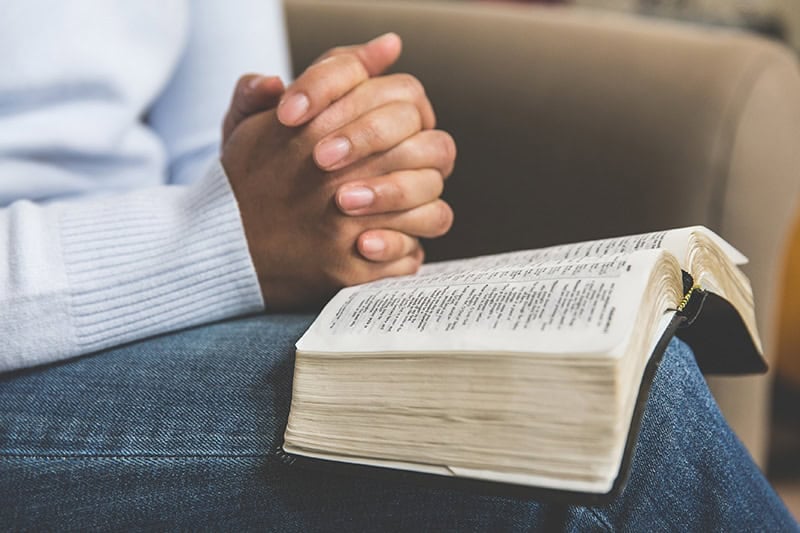 A Christian woman's hands folded in her lap with an open Bible