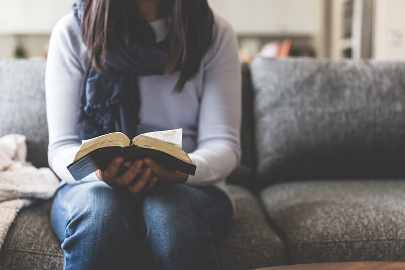 A Christian woman sitting on a couch reading the Bible
