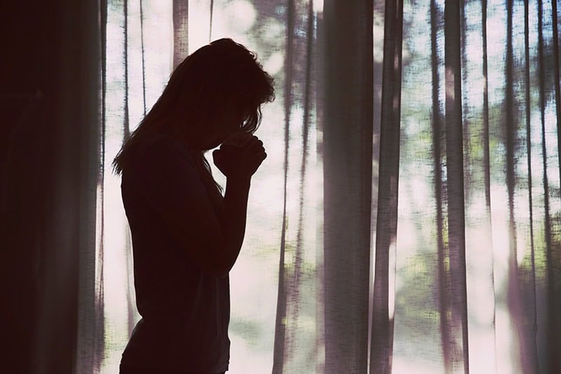 Silhouette of a Christian woman bowing her head in prayer as she tries to surrender control to God