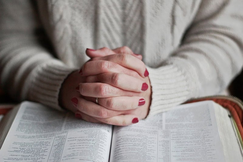 A Christian woman's hands folded on top of her open study Bible