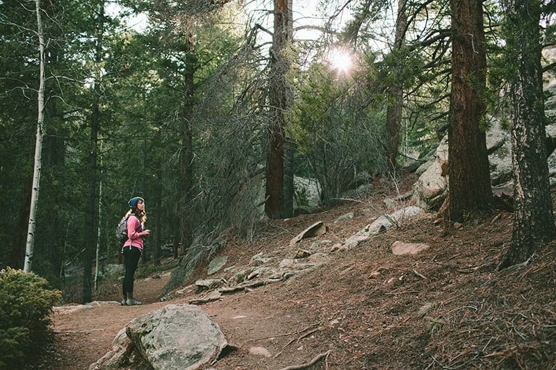 A Christian woman on a path in the forest, looking up a rocky hill