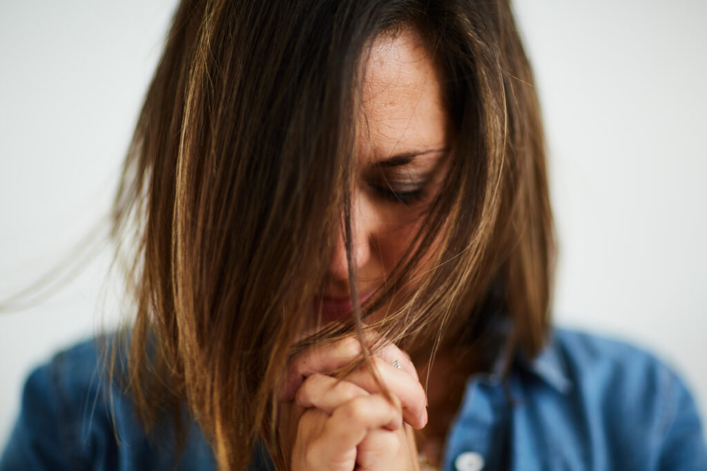 A Christian woman bowing her head and folding her hands in prayer to deepen her relationship with God