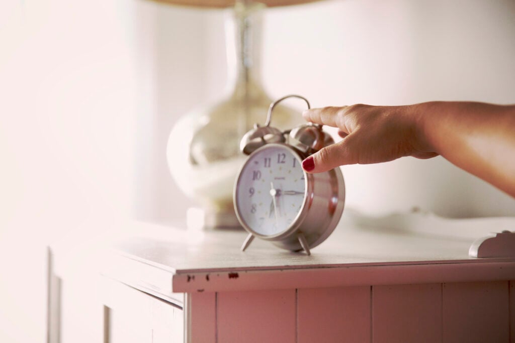 A Christian woman reaching for the alarm clock on her bedside table