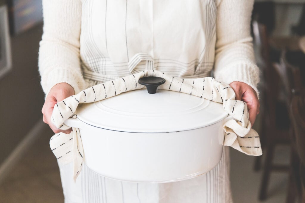 A Christian woman in a white apron carrying a hot white Dutch oven