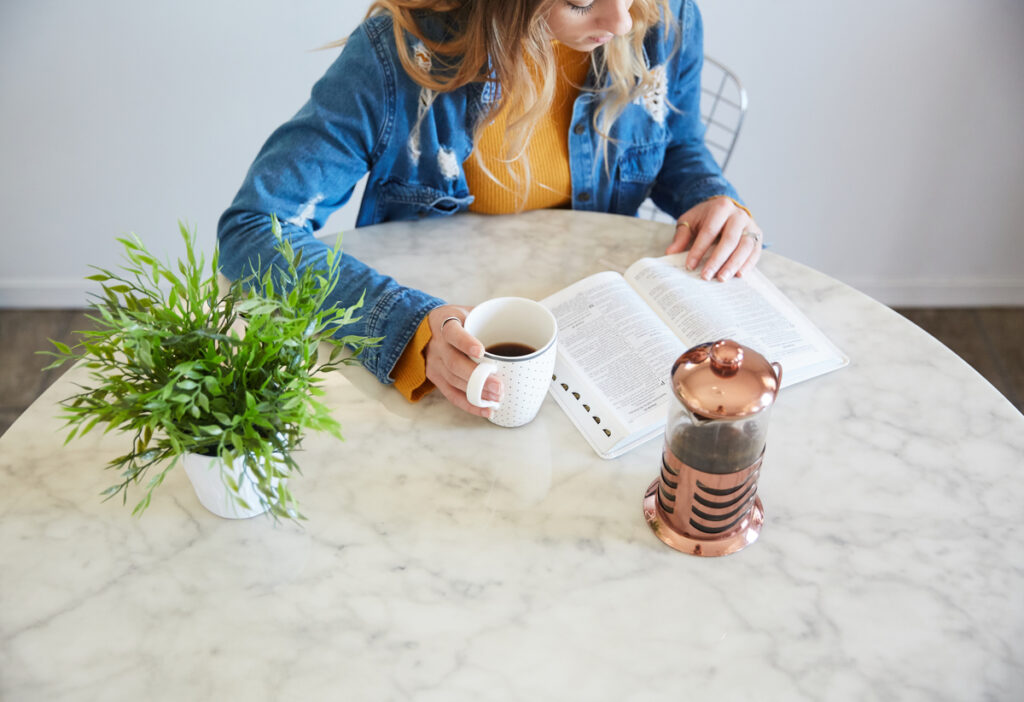 A Christian woman practicing rhythms of grace with a Bible open on her table and a cup of coffee in her hand