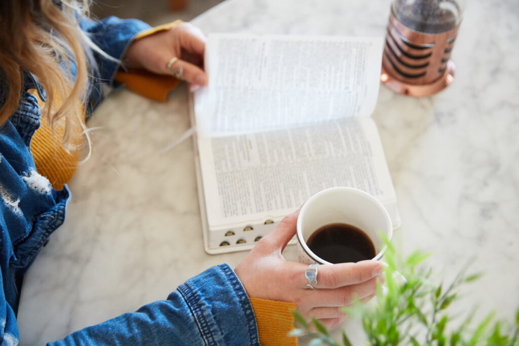 A Christian woman reading her Bible with a mug of coffee beside her as she practices the rhythms of grace