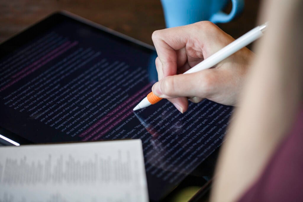 A Christian woman doing a personal Bible study on a digital tablet using a stylus