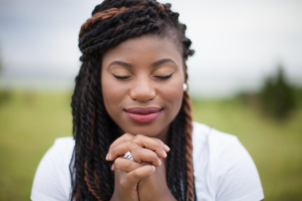 A Christian woman with her eyes closed and hands folding in prayer