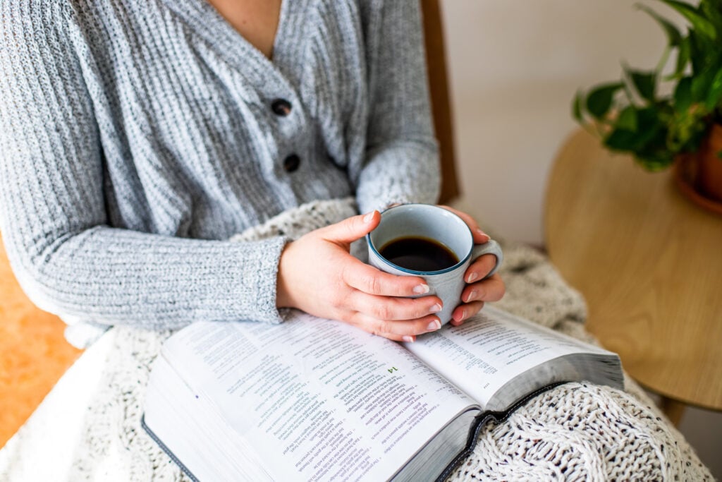 A Christian woman with an open Bible in her lap, holding a mug of black coffee, meditation on the Bible's love story