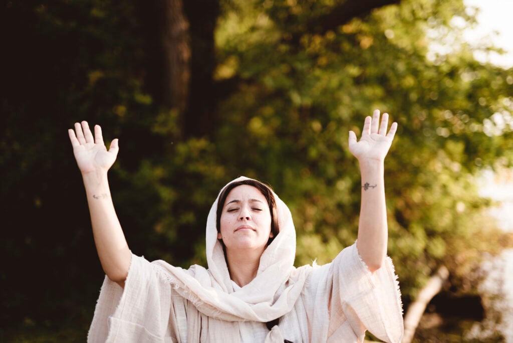 A woman dressed in ancient biblical clothing raising her arms in praise to God