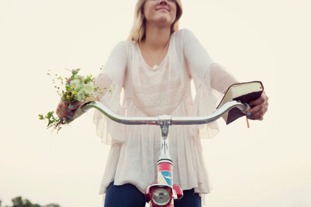 A Christian woman experiencing the power of praise by riding a bicycle to pick wildflowers on her way to read her Bible in nature