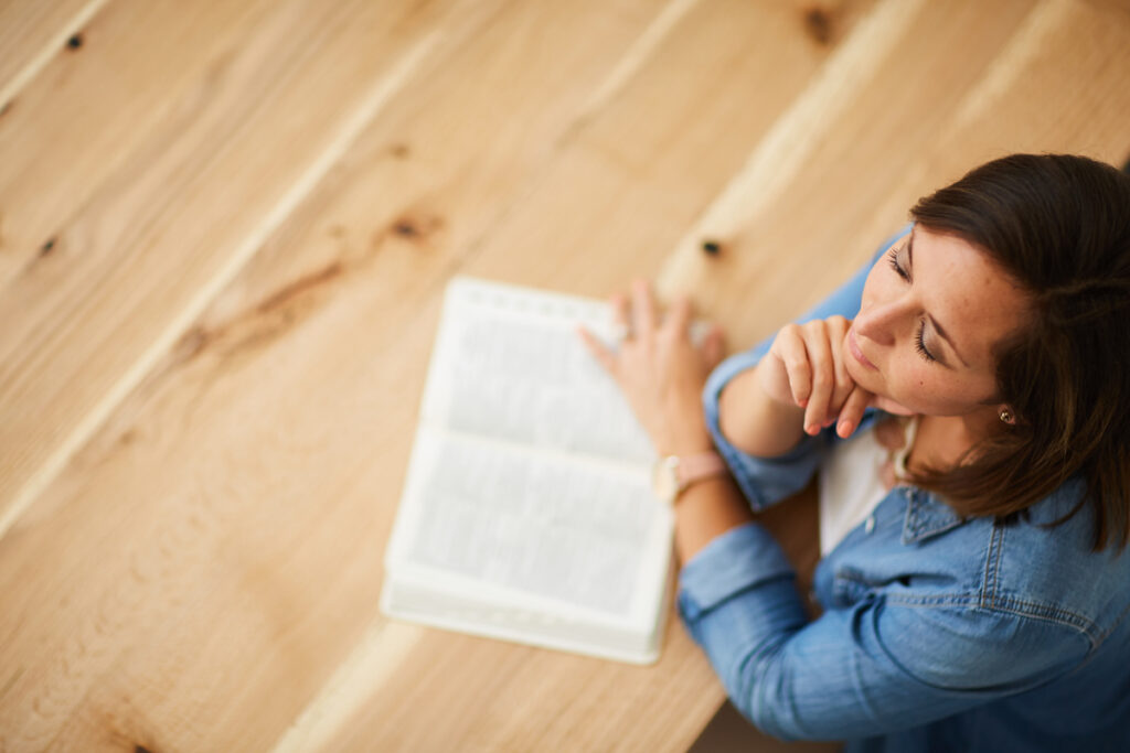 A Christian woman meditating on Scripture with a Bible open on the table in front of her