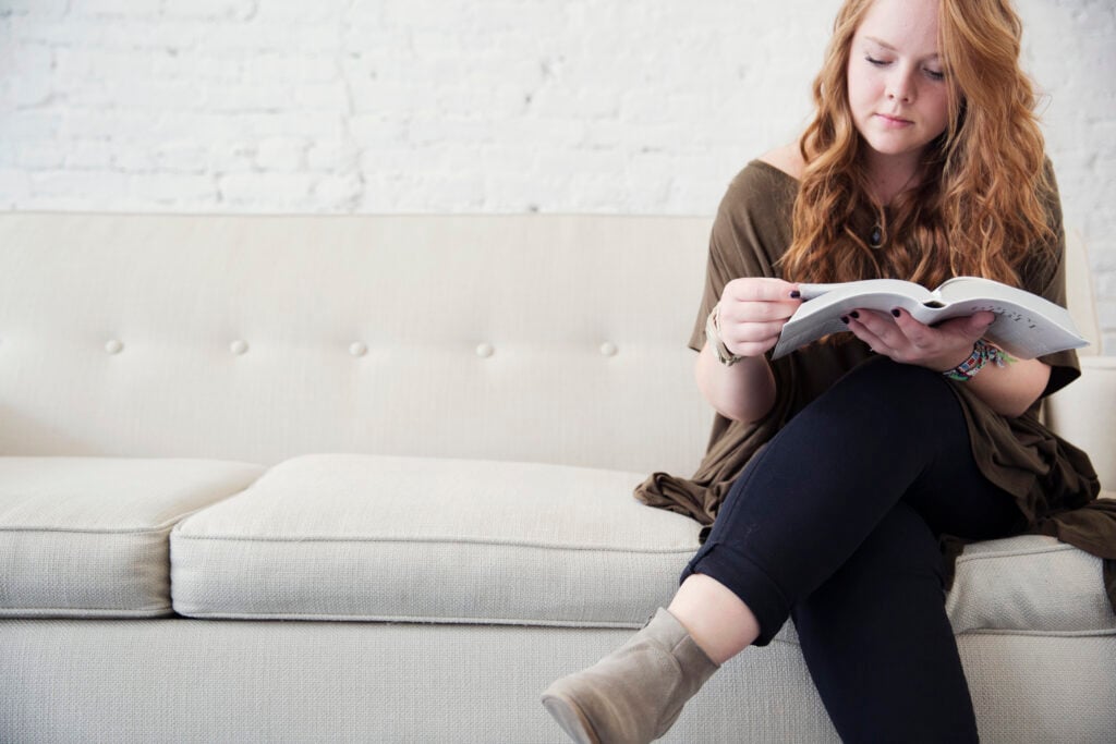 A young Christian woman sitting on a white couch and reading the Bible