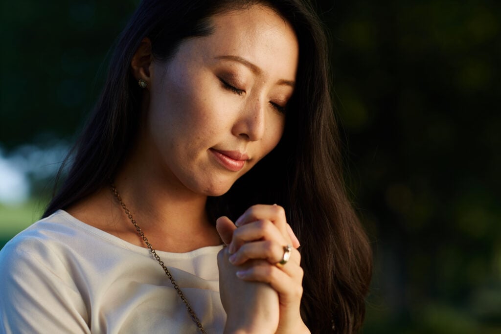 A Christian woman with her eyes closed and hands folded in prayer 