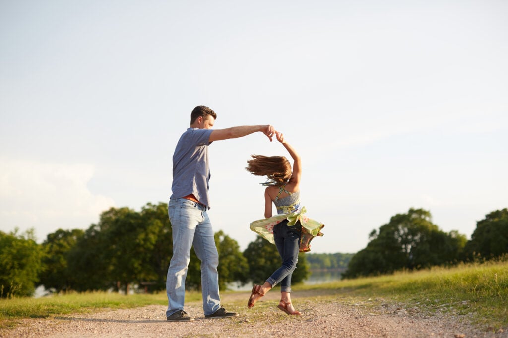 A Christian father twirling his young daughter in a dance on a sunlit, dirt road