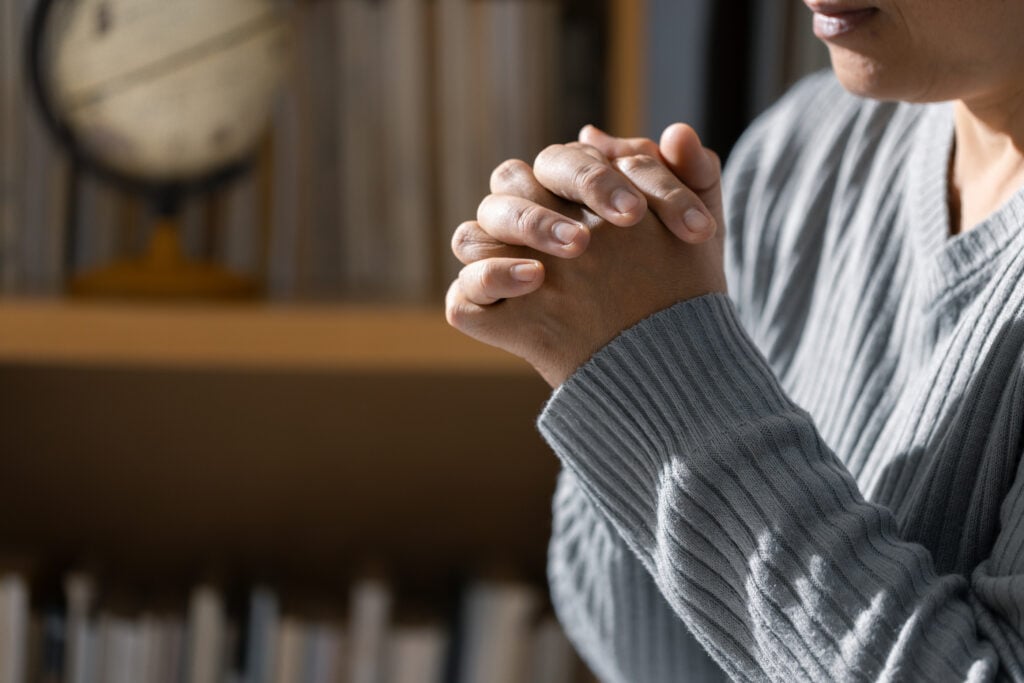 A Christian woman with her hands folded in prayer to calm her anxiety