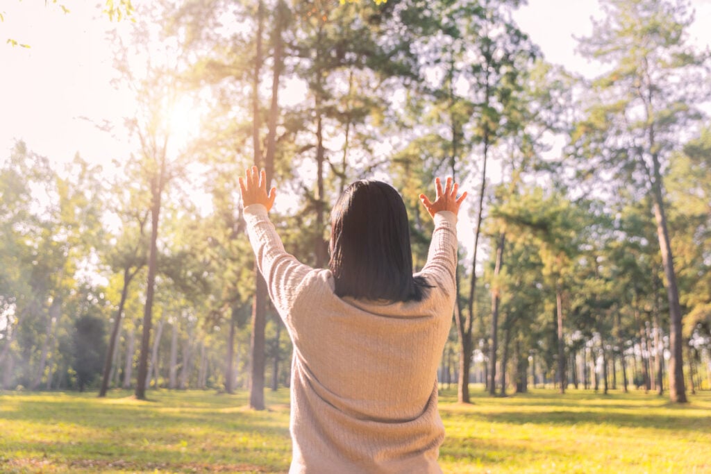 A Christian woman with her hands raised in worship as she looks up toward the sun