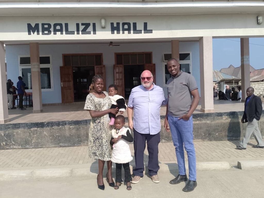 A Christian family in Tanzania standing with a friend in front of Mbalizi Hall