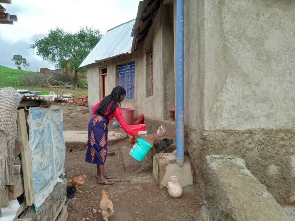 A Christian woman in Tanzania feeding her chickens in her dirt yard as she's waiting on God in difficult times