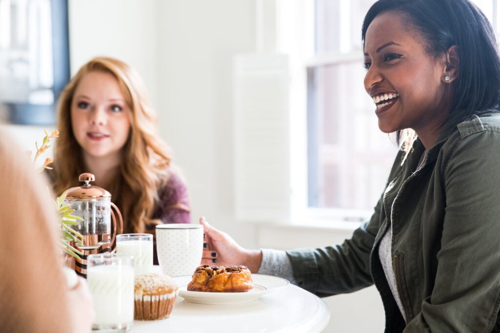 Two Christian women at a dining table practicing biblical hospitality and curiosity by listening attentively as a friend talks