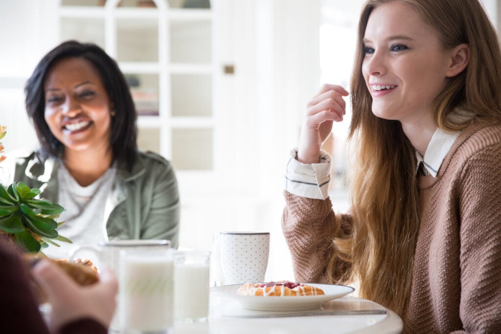 Two Christian women at a dining table practicing biblical hospitality and curiosity by listening attentively as a friend talks