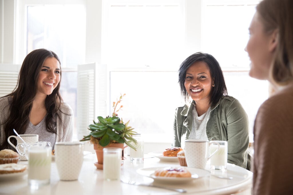 Two Christian women at a dining table practicing biblical hospitality and curiosity by listening attentively as a friend talks