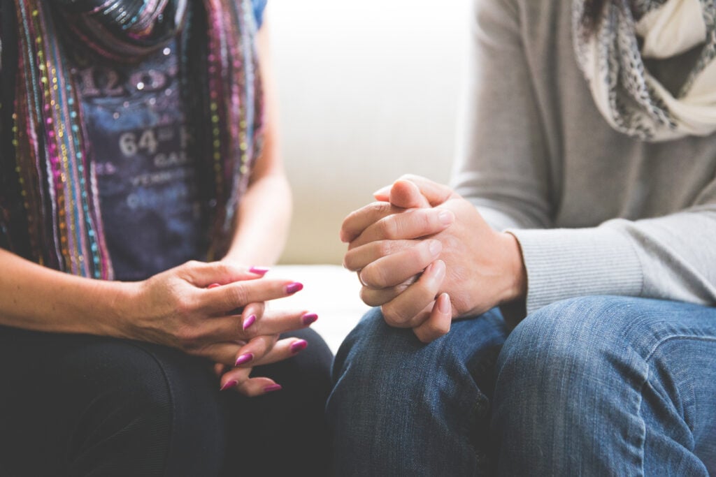 Two Christian woman sitting beside each other with their hands folded as they ponder the live at peace with everyone meaning