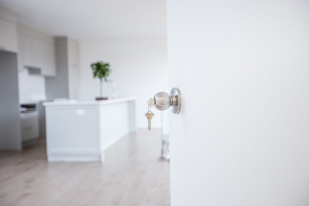 A close-up of a front door knob with the key still in it, with the interior of a new home blurred in the background