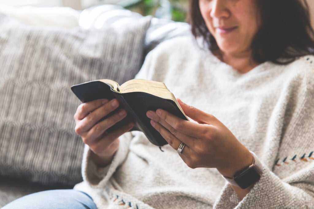 A Christian woman sitting on a couch while reading a small, black Bible