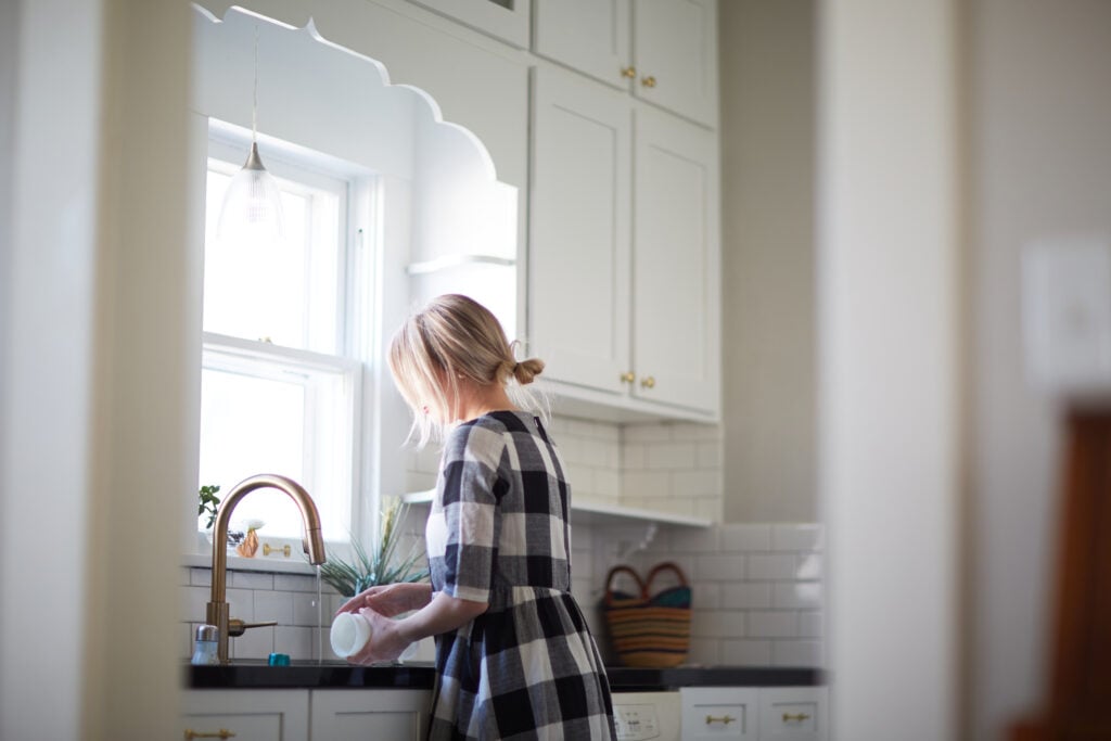 A Christian woman in a navy and white checkered dress practicing biblical stewardship as she washes dishes