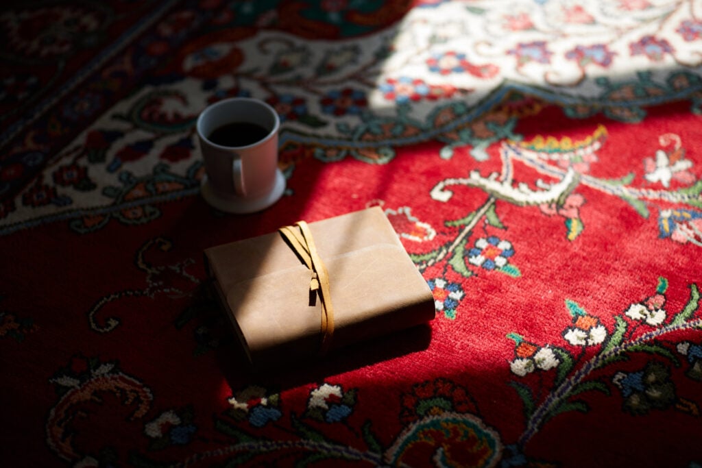 A dark red persian rug with a leather-bound Bible and a mug of coffee